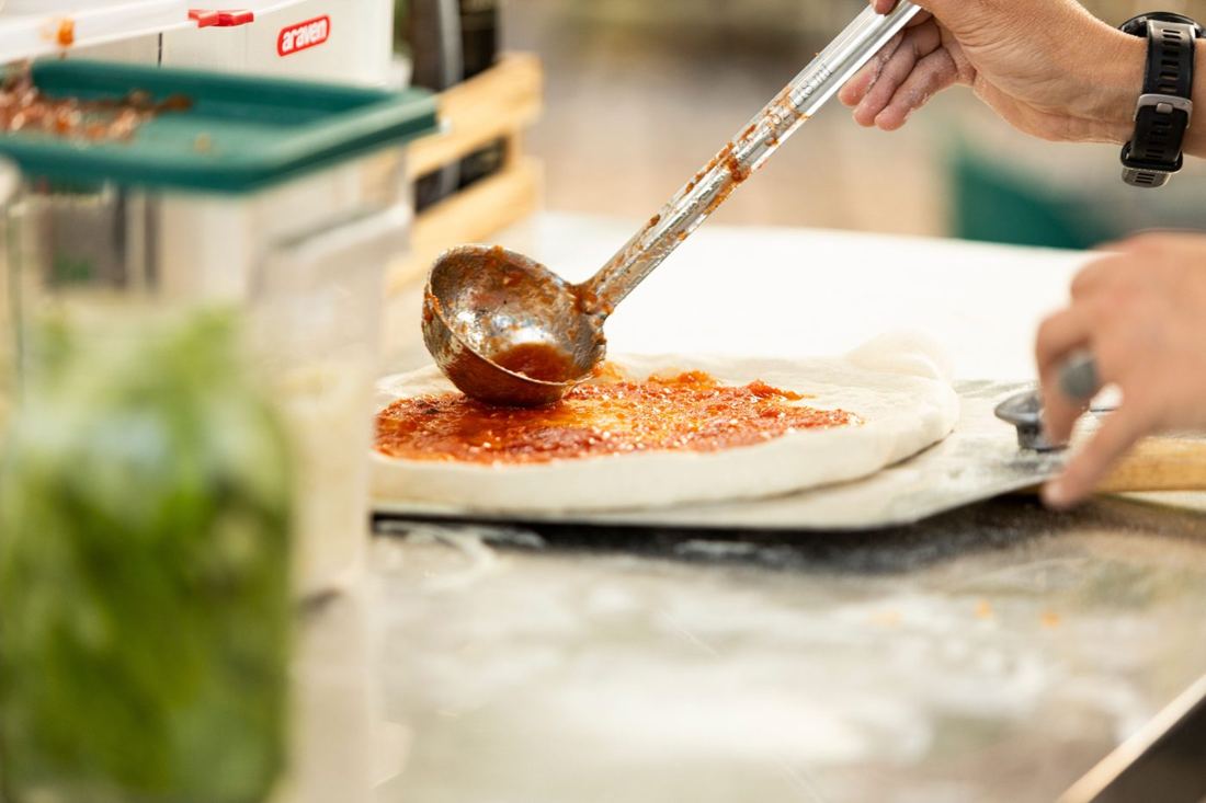 Ladling tomato sauce onto fresh pizza dough on a peel