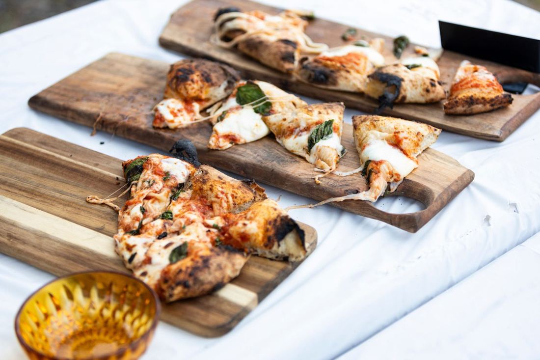 Slices of wood-fired margherita pizza with stretchy cheese on wooden serving boards