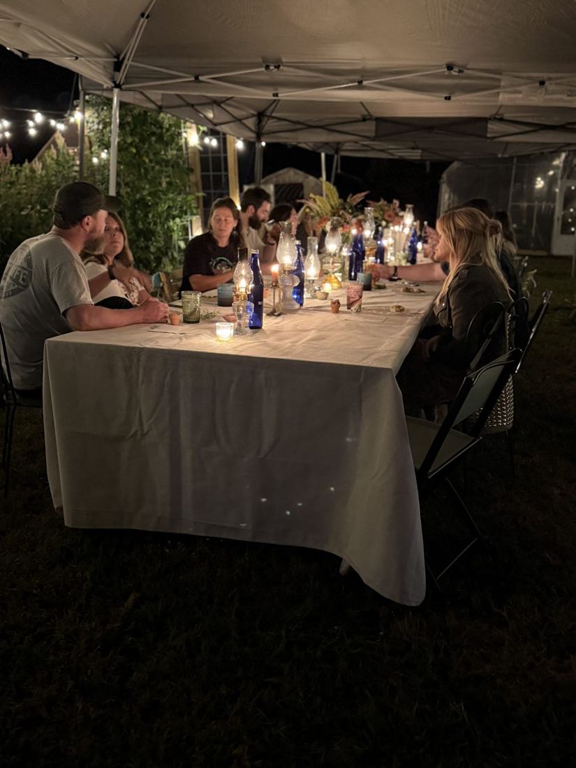 Guests gathered at the long candlelit family-style table at night under string lights