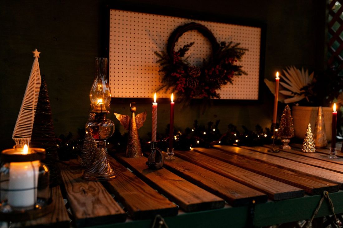 The potting bench lit with tapers, an oil lamp, a brass angel and a berry wreath