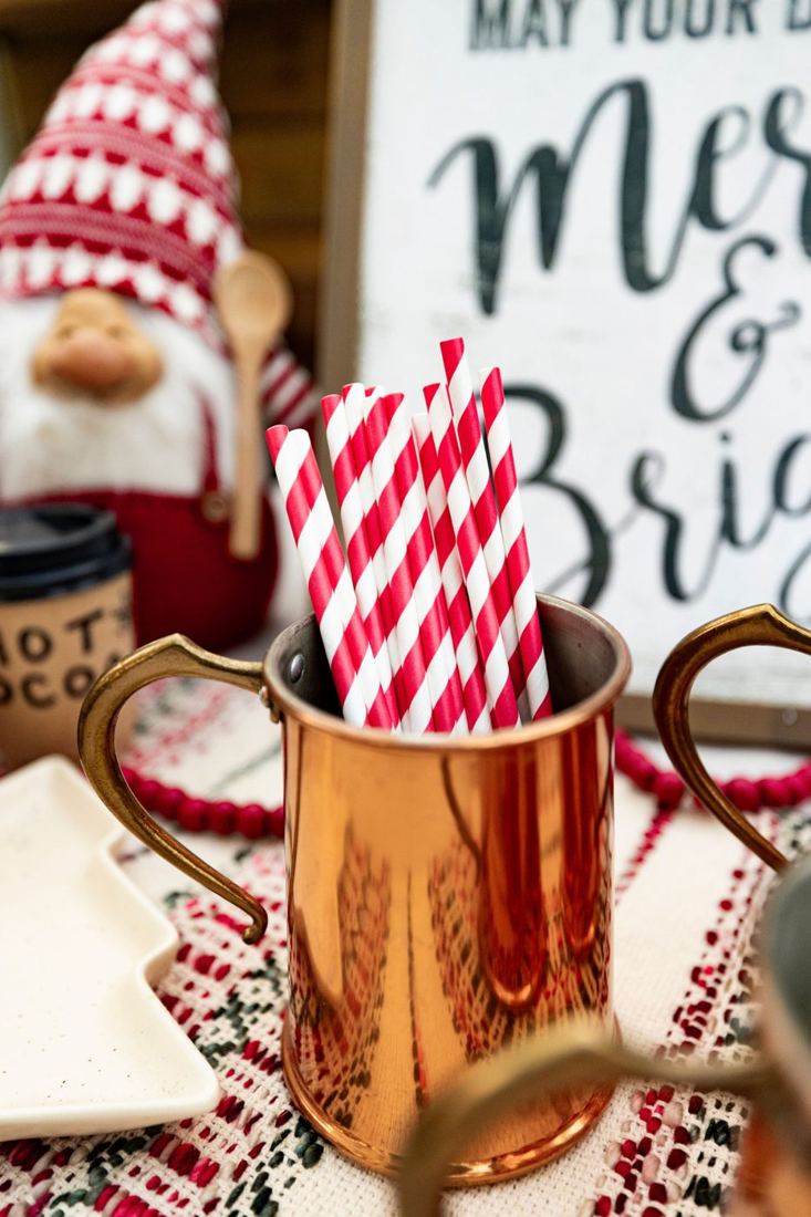 Red and white striped straws in a vintage copper mug on a woven runner